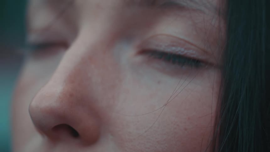 A teenage girl is outside looking up and she closes her eyes