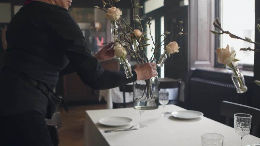 Woman with black t shirt and hoop earrings lays long table in the restaurant