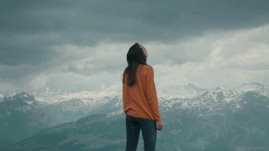 A woman watches a bird fly overhead while overlooking a mountain range