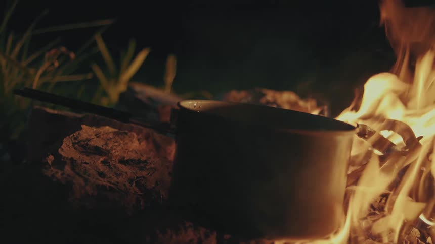 Camping person places pot on the campfire