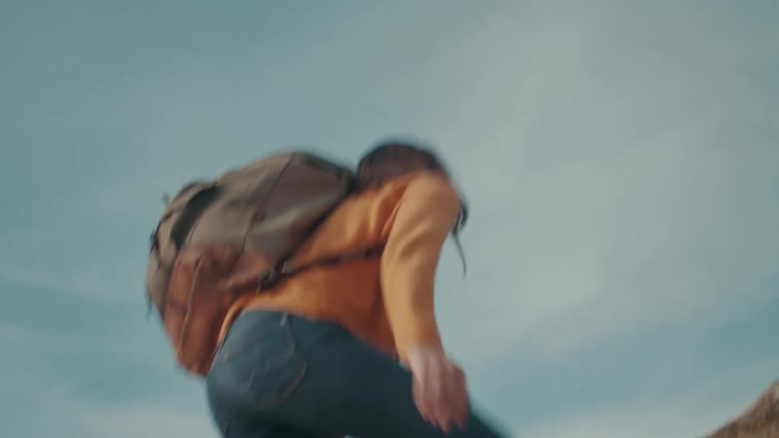 A woman wearing a camping backpack takes careful steps while hiking up a mountain