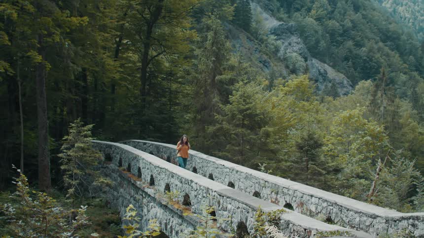 A woman crosses the bridge near the hills