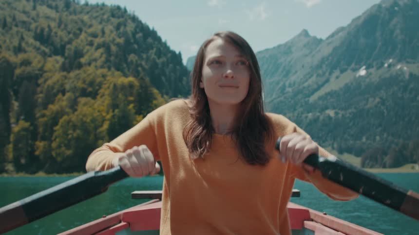 A woman rows a boat across a lake in a mountain valley during the day