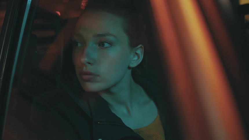 A woman likes out of the window while riding in the passenger seat of a car at night