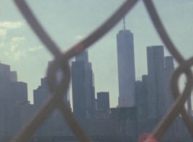 A city skyline is visible through a chain link fence
