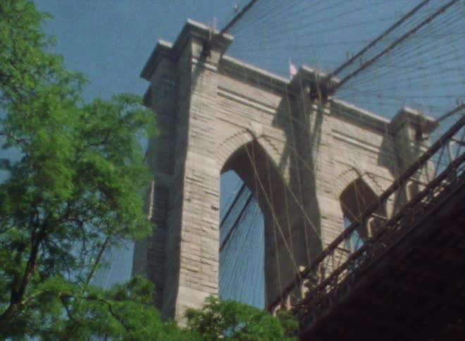 Tower arches at center of suspension bridge tower over nearby trees under a clear blue sky