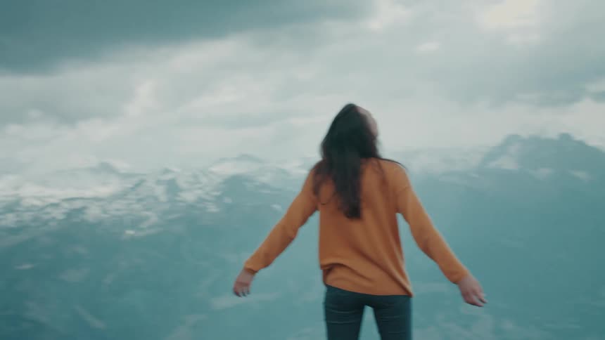 A woman stands atop a mountain ridge with her arms outstretched