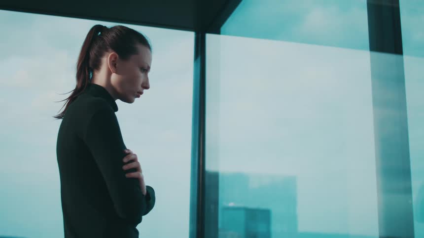 A sad looking woman looks out an office window