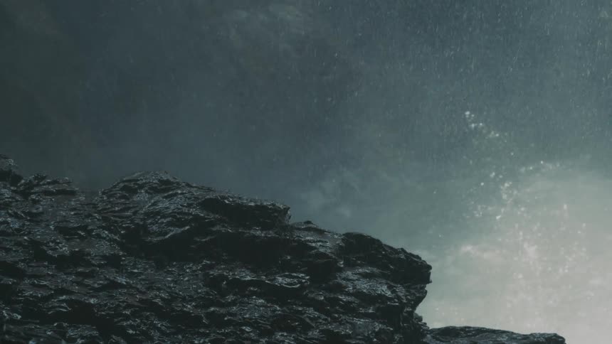 Water crashing up against rocks as mist from the water rises over the boulders