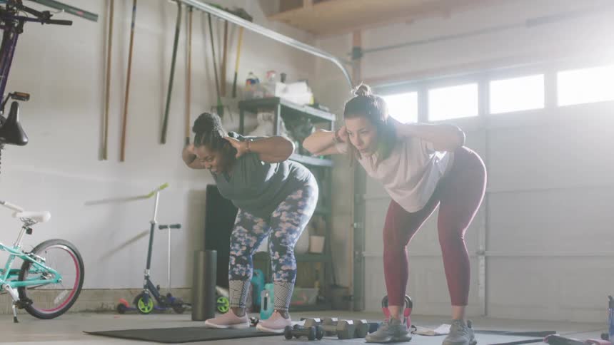 Two women bend down while working out in a home garage
