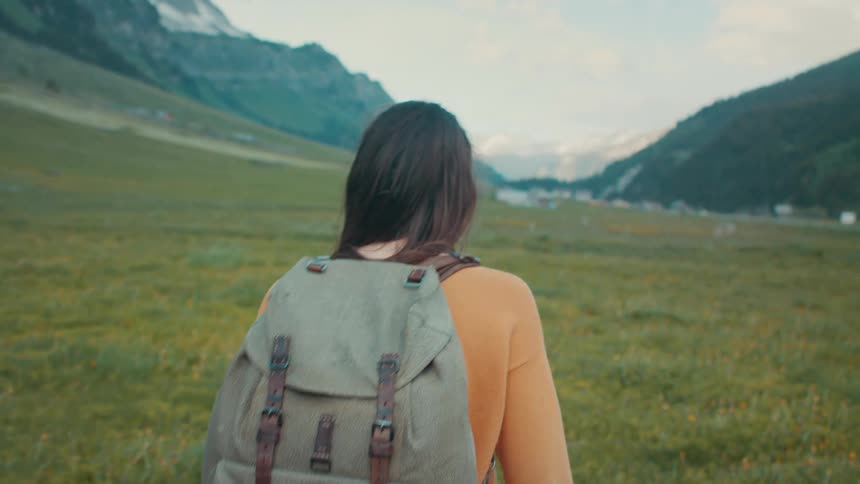 A woman hikes through a field below a mountain range