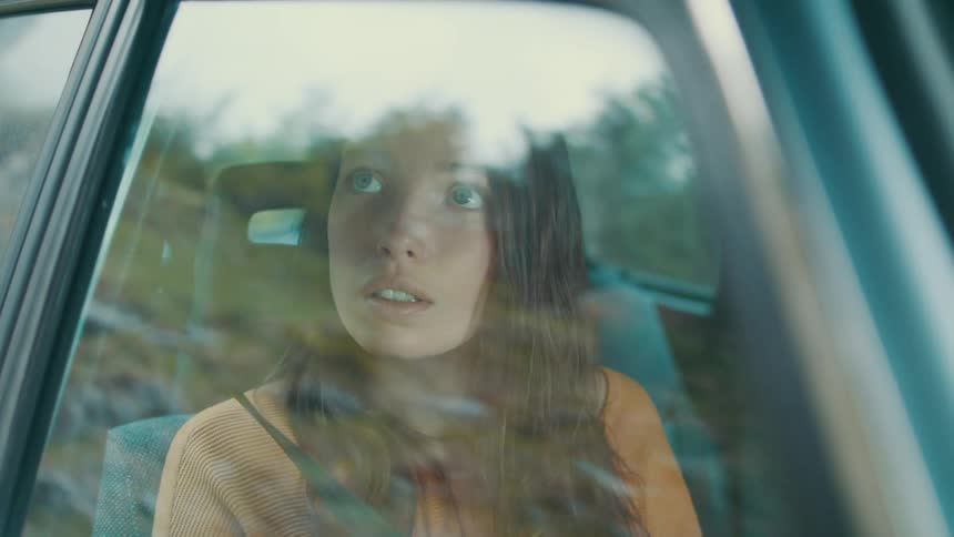 A teenage girl sits in a passenger seat in a car and looks out the window