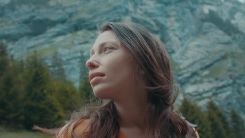Female backpacker looks upward and around near forest sitting at base of mountain