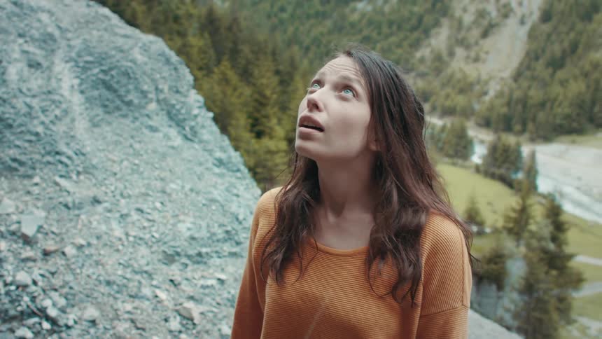 A woman takes deep breaths and looks upwards after hiking up a mountain side