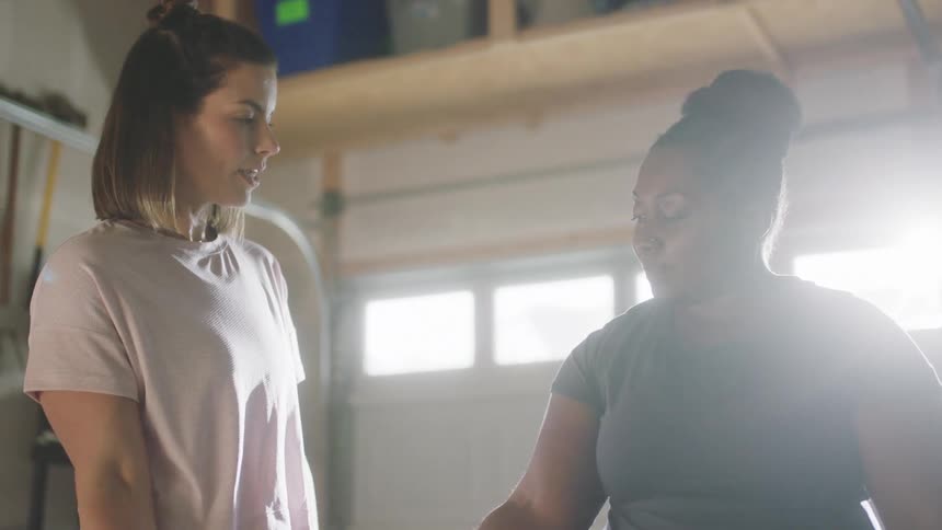Fitness trainer guides another woman trough exercises while they stand in garage