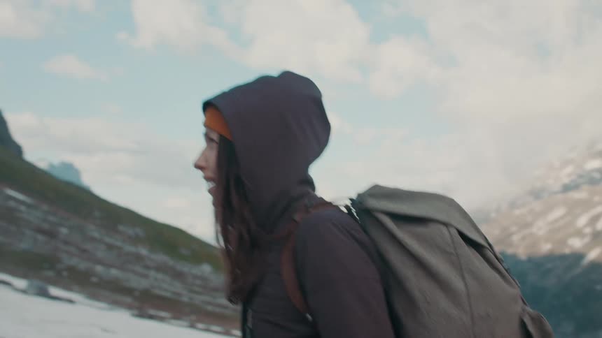 A woman hikes up the side of a snow capped mountain