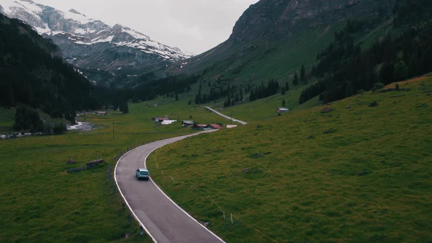 A vehicle travels along a winding road through a mountain valley during the day