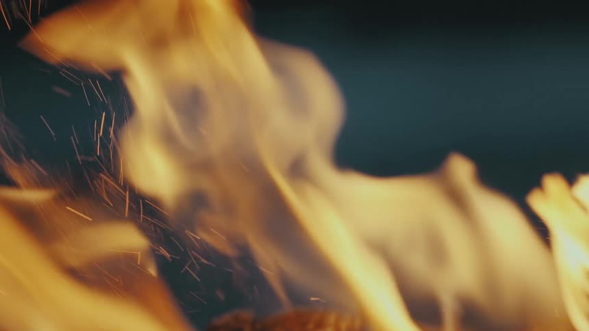 A fire burns vigorously while it releases embers into the night sky