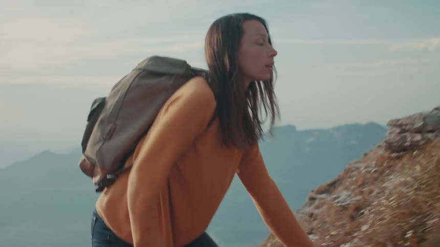 A woman wearing an orange sweater wearing a backpack hiking up a steep mountain