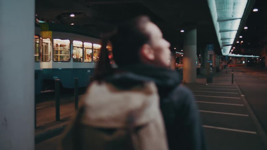 A woman wearing a tan backpack walks quickly while a subway train rolls by on her left