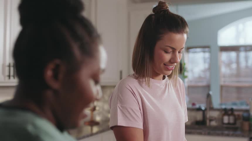 Two women laugh and chat while standing in the kitchen