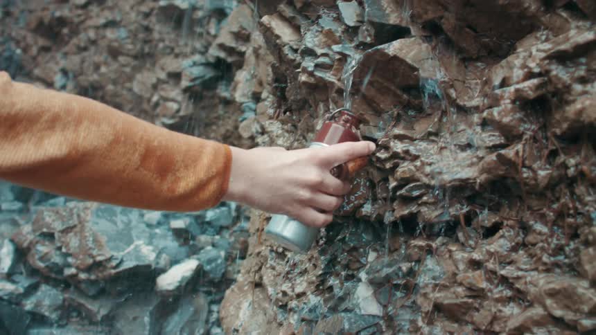 A person reaching their water bottle under water trickling down rocks