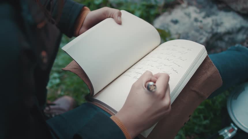 A woman writes in a journal while sitting outdoors during the day