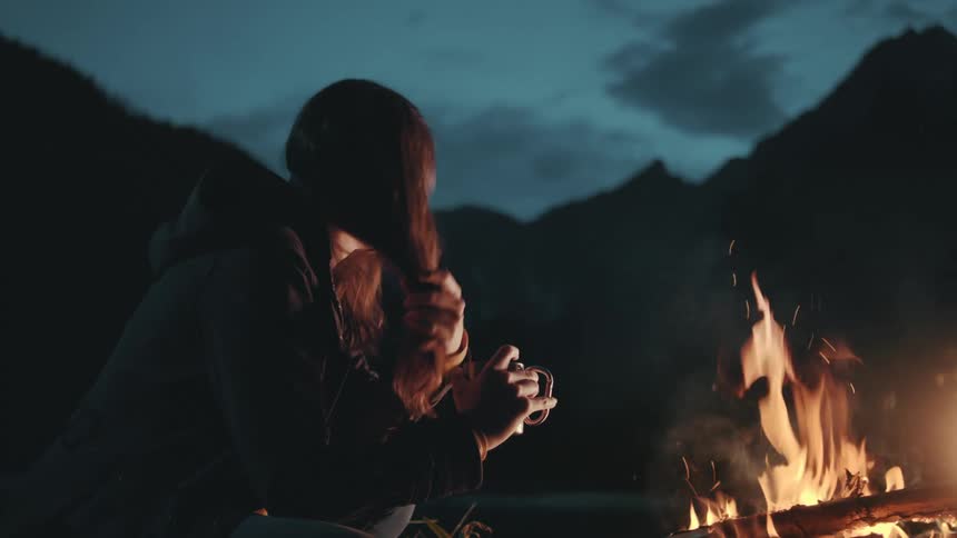A woman is drinking by the campfire