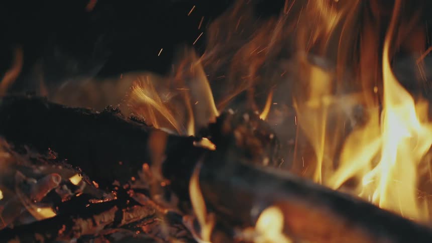 A campfire fueled by several pieces of wood burns and releases embers