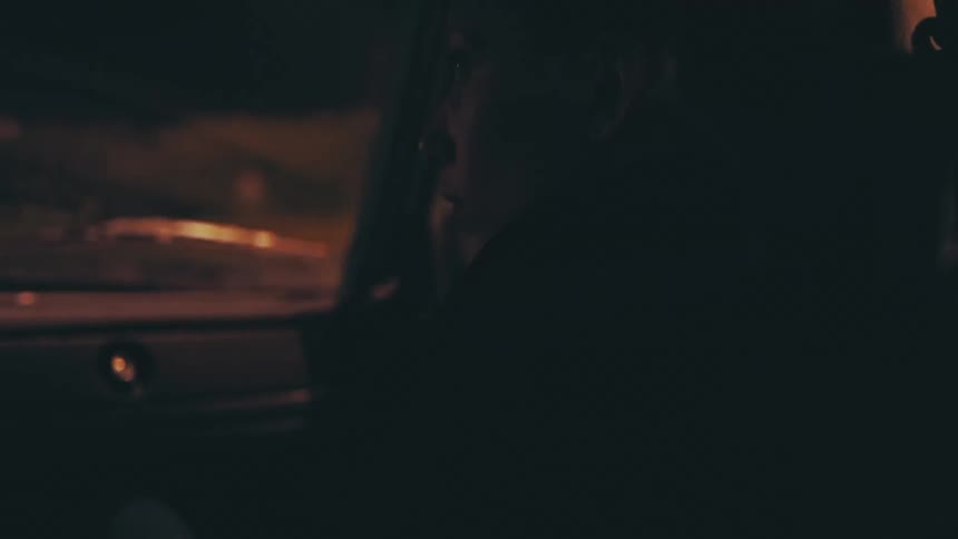 A woman sits in the passenger seat of a vehicle as it drives down a street at night