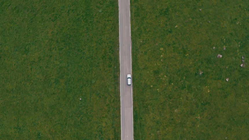 An automobile is traveling on a rural road surrounded by grass and scattered rocks and boulders