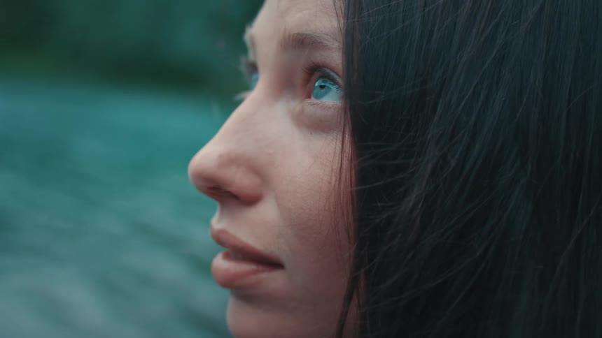 Dark haired blue eyed woman on riverbank looks upward