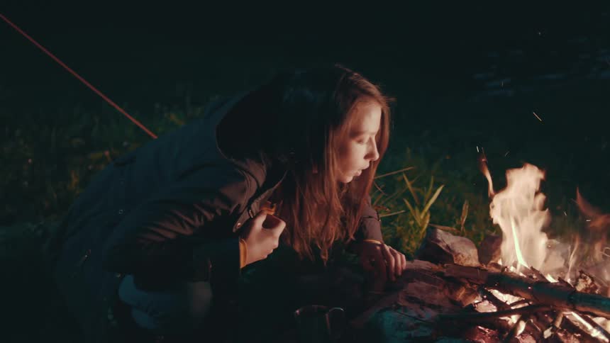 A woman blowing on a campfire to keep it going