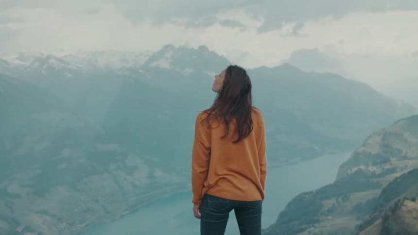 A woman standing high in the mountains watches a bird as it flies by