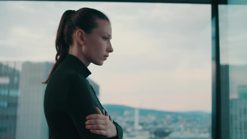 A woman wearing a black sweater standing looking out solemnly with her arms crossed