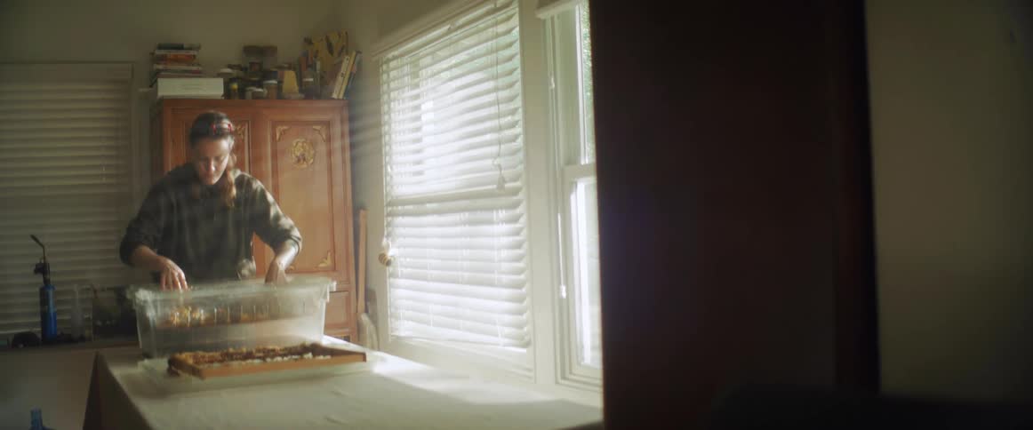 A person is using their hands to move things around in a plastic tub that is on a table in a room with a blindcovered window and a wardrobe