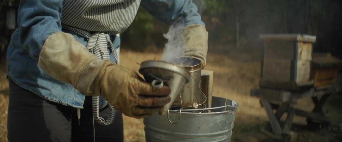 A beekeeper using smoke and a metal tin outdoors