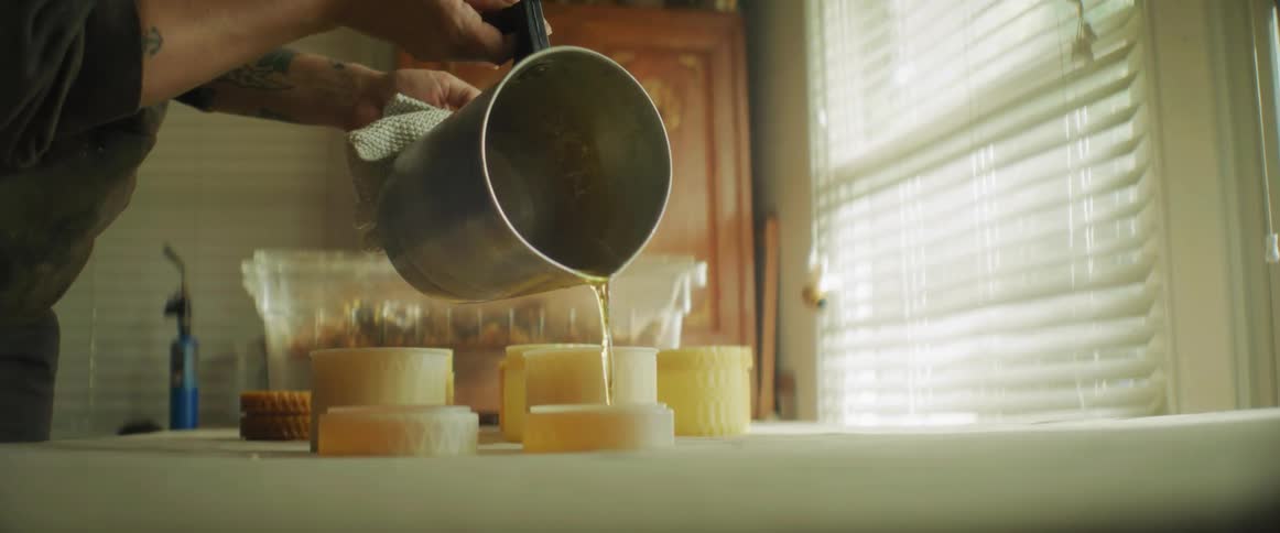 Woman pours liquid beeswax on translucent containers