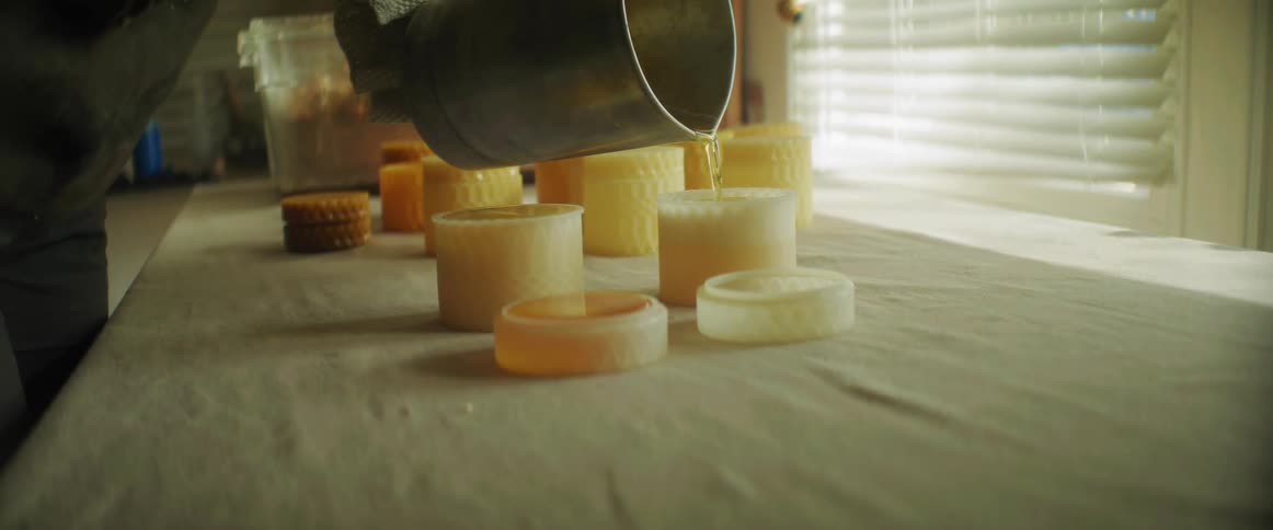Woman pours liquid beeswax on small translucent containers