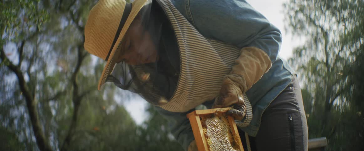 An white woman is outdoors with some bees in the day time