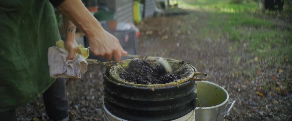 A person is mixing a substance and sifting it through a screen into pot below