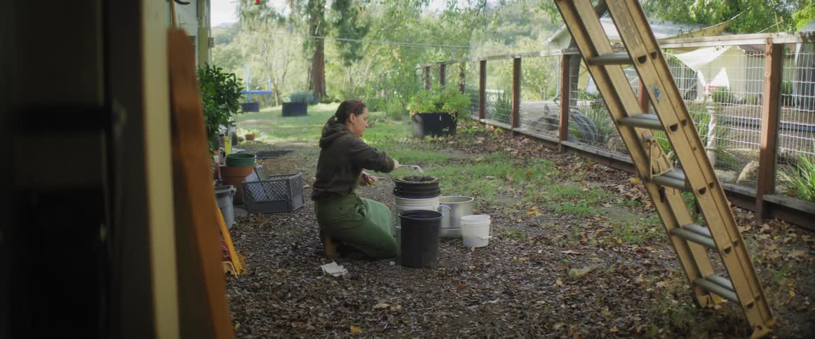 A woman knelt down stirring in a black bucket