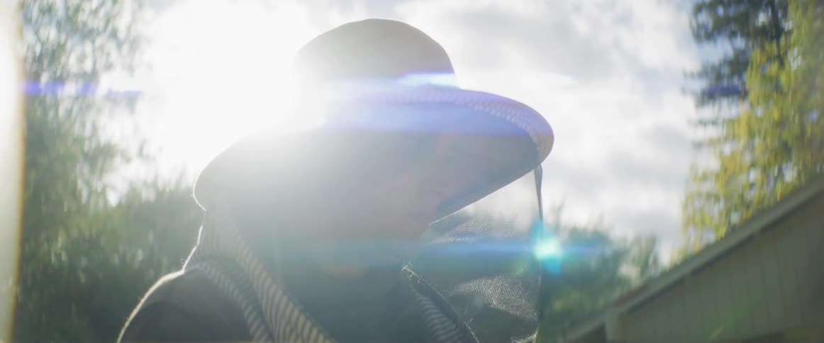 A woman is standing outdoors as a beekeeper