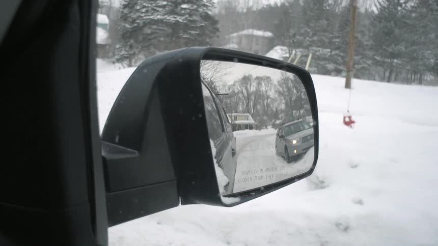Cars in snow as seen in a side view mirror on a snowy winter day
