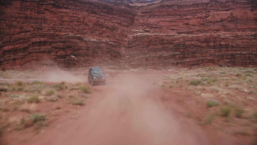 Car drives on dirt road in a deep valley with very steep sides