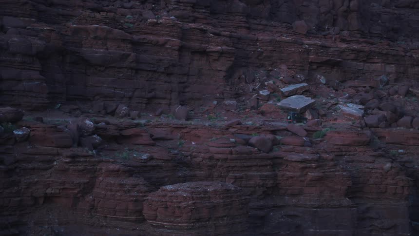 A vehicle drives along the edge of a rock formation