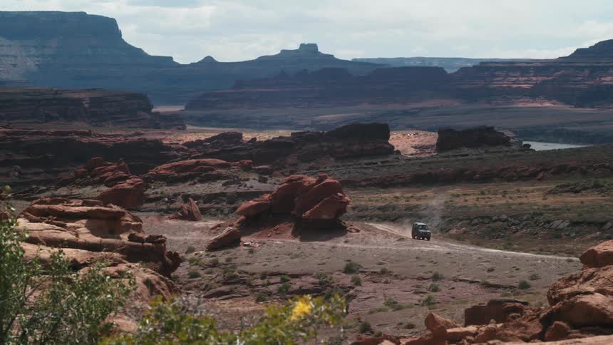 A vehicle drives on a dirt road in front of a canyon