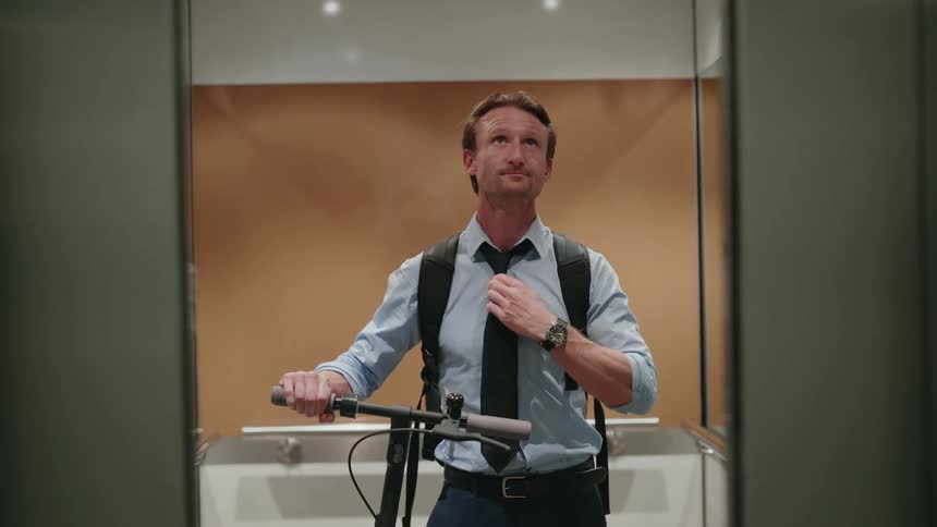 Man standing in elevator with e scooter as doors close checks wristwatch
