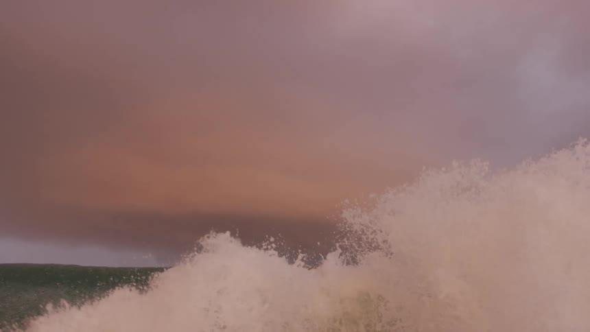 Waves roll in and splash high in a dark pink sky