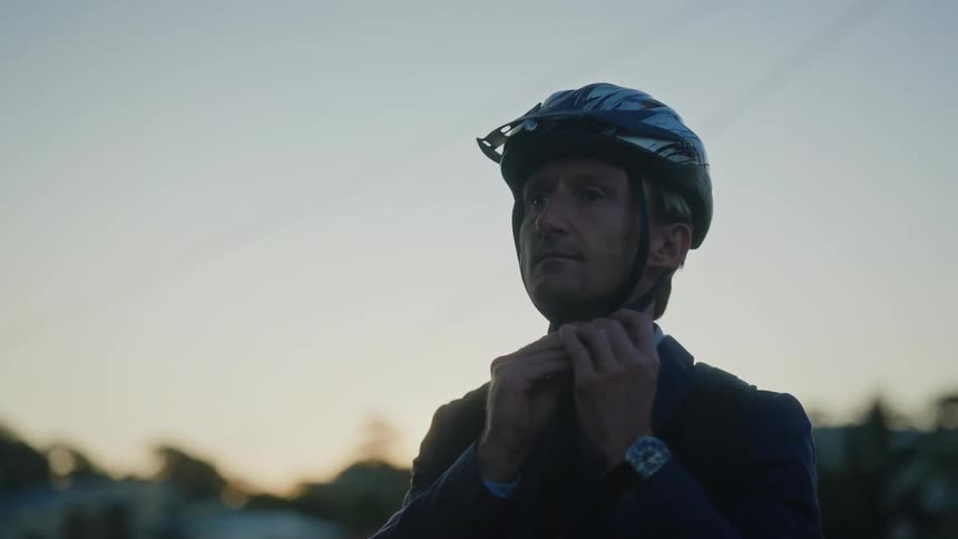 A man puts on a bike helmet and checks behind him before riding off